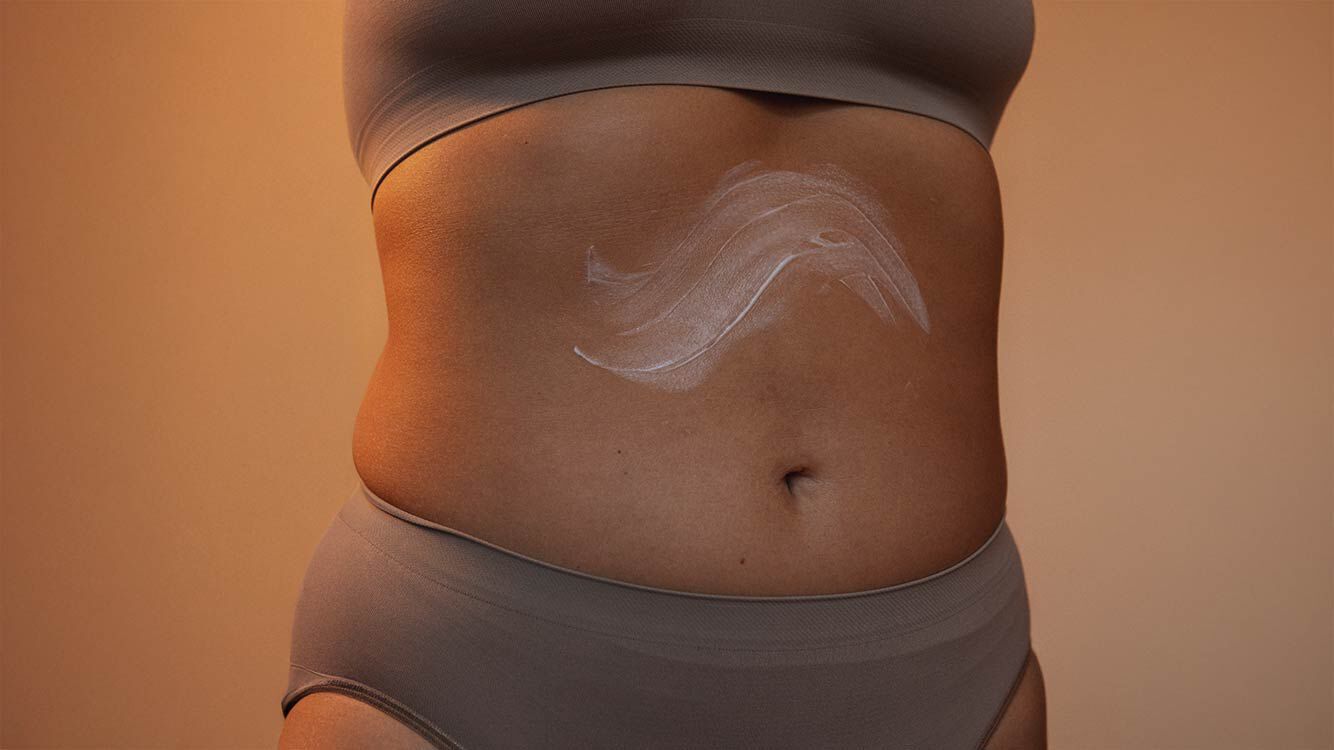 Close-up van de buik van een vrouw met cr&egrave;me erop.